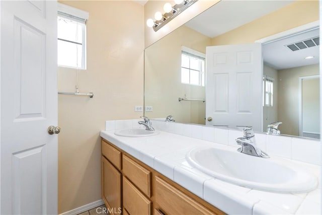 full bath featuring a sink, visible vents, baseboards, and double vanity