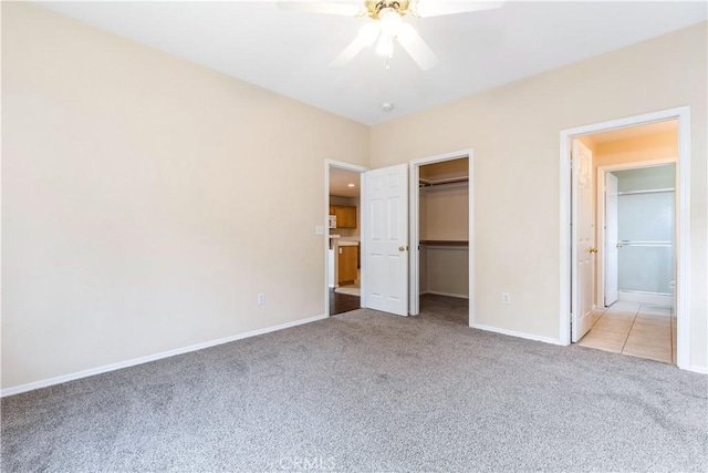 unfurnished bedroom with a closet, carpet, baseboards, ceiling fan, and a spacious closet