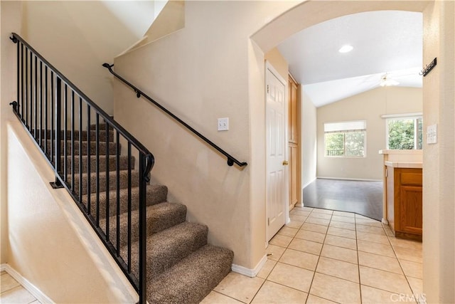 staircase featuring tile patterned flooring, arched walkways, baseboards, and vaulted ceiling