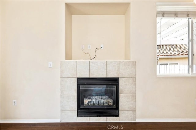 details with baseboards, wood finished floors, and a tiled fireplace