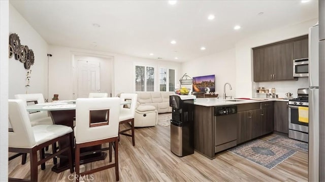 kitchen featuring a sink, open floor plan, stainless steel appliances, dark brown cabinetry, and light wood finished floors