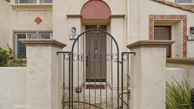 property entrance with stucco siding, fence, and a gate