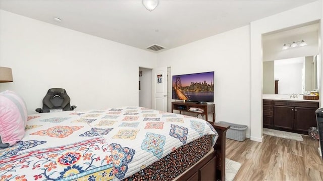 bedroom featuring ensuite bath, visible vents, light wood finished floors, and a sink