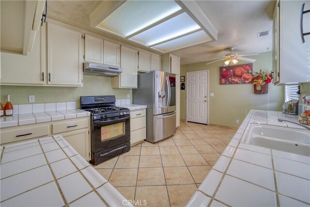 kitchen with black range with gas stovetop, stainless steel fridge with ice dispenser, under cabinet range hood, tile countertops, and a sink