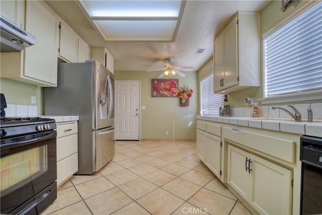 kitchen featuring ceiling fan, under cabinet range hood, tile countertops, light tile patterned floors, and black appliances