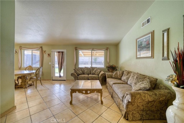 living area featuring visible vents, a textured ceiling, light tile patterned flooring, and vaulted ceiling