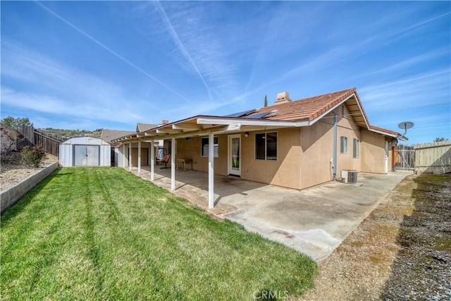 back of house featuring an outbuilding, a fenced backyard, stucco siding, a storage unit, and a patio area