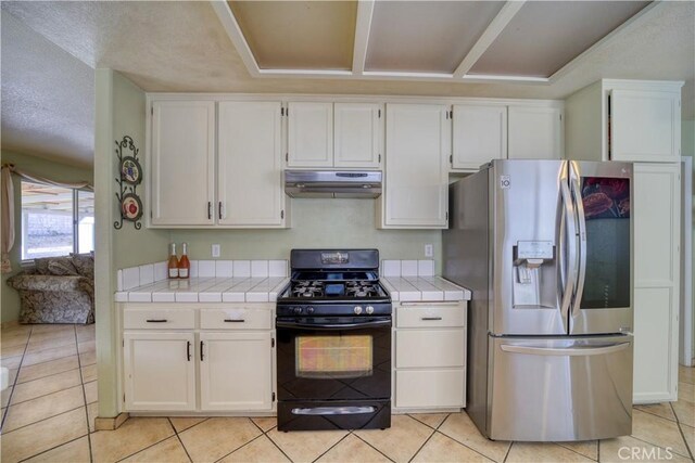 kitchen featuring under cabinet range hood, tile countertops, stainless steel fridge, white cabinets, and black range with gas cooktop