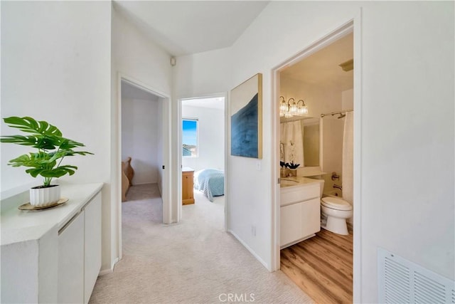 hall featuring visible vents, light colored carpet, and baseboards