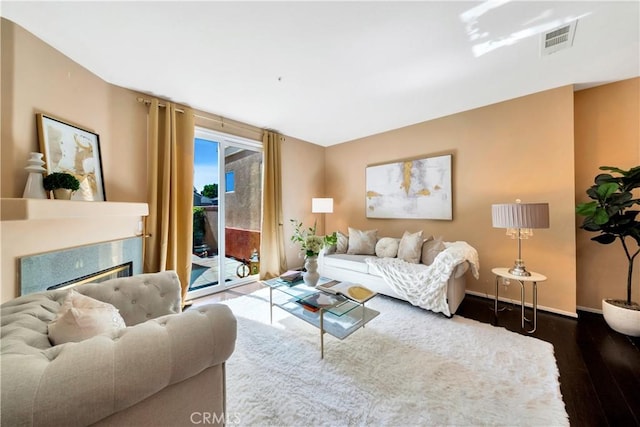 living room featuring a premium fireplace, baseboards, visible vents, and wood finished floors