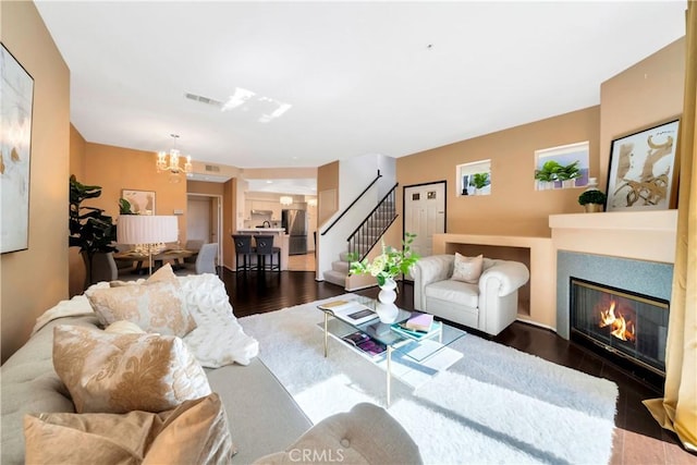 living area with stairs, a chandelier, a glass covered fireplace, and wood finished floors