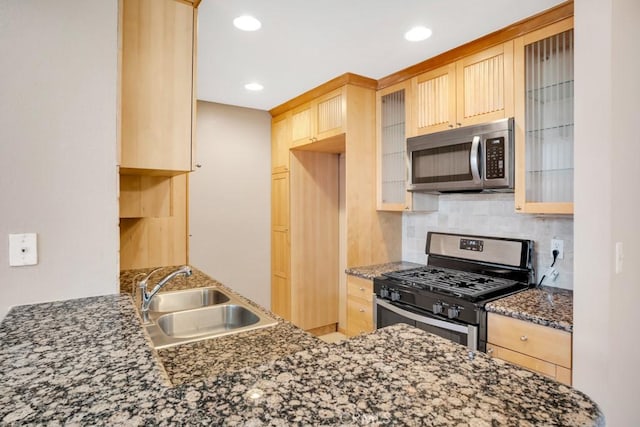 kitchen with dark stone countertops, light brown cabinets, a sink, stainless steel appliances, and backsplash