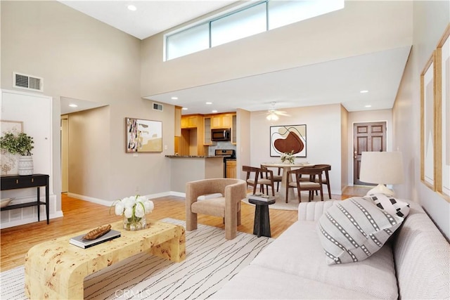 living room featuring a high ceiling, baseboards, visible vents, and light wood-type flooring