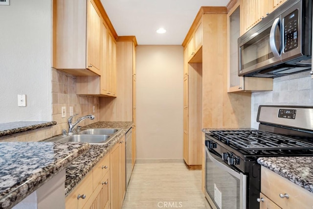 kitchen featuring light brown cabinetry, stainless steel appliances, glass insert cabinets, and a sink