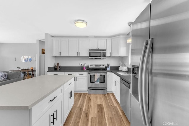 kitchen with light wood finished floors, dark countertops, decorative light fixtures, stainless steel appliances, and white cabinetry