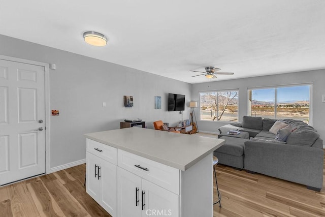 kitchen featuring a kitchen island, open floor plan, a kitchen breakfast bar, light wood-style floors, and white cabinets