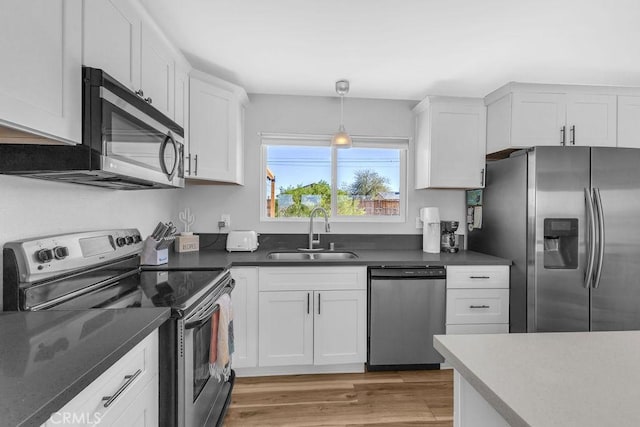 kitchen featuring light wood finished floors, a sink, white cabinets, appliances with stainless steel finishes, and dark countertops