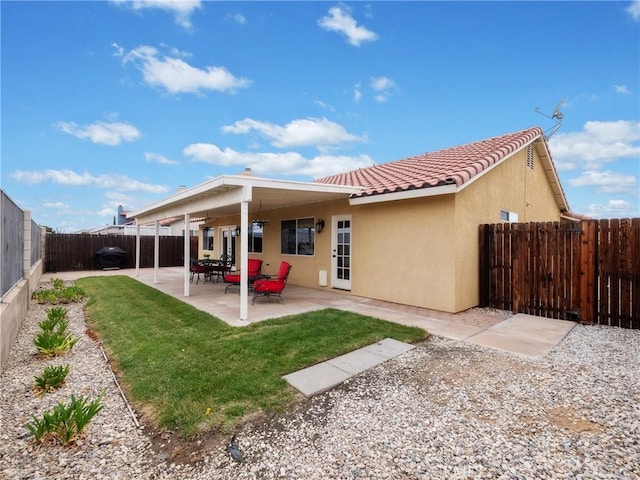 back of house with stucco siding, a lawn, a fenced backyard, a patio area, and a tiled roof