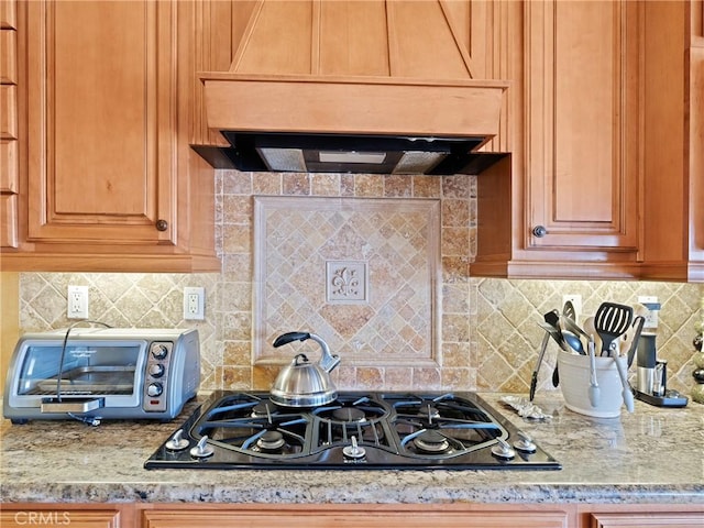 kitchen with light stone counters, decorative backsplash, gas stovetop, and wall chimney range hood