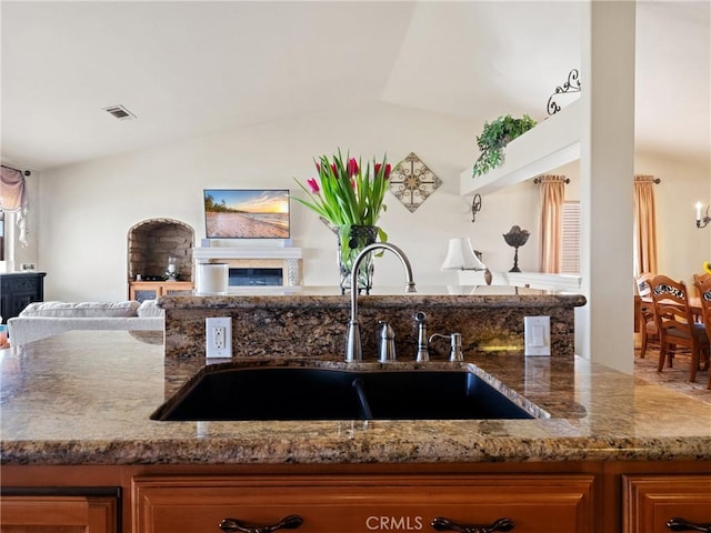 kitchen with visible vents, a sink, open floor plan, stone counters, and vaulted ceiling