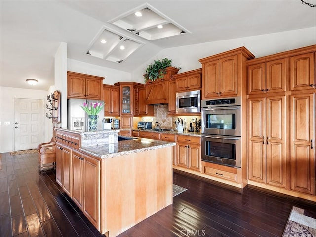 kitchen with a center island, glass insert cabinets, light stone counters, dark wood-style floors, and stainless steel appliances