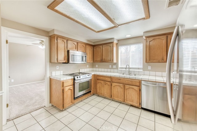 kitchen with tile counters, light colored carpet, light tile patterned floors, appliances with stainless steel finishes, and a sink