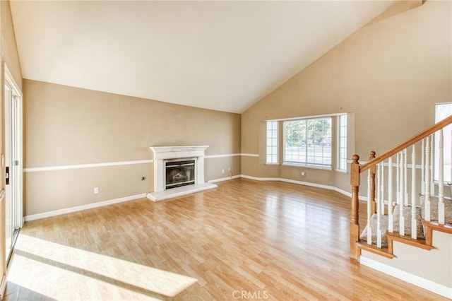 unfurnished living room with a glass covered fireplace, light wood-style flooring, stairs, and baseboards