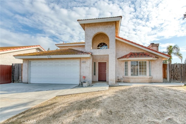 mediterranean / spanish house featuring a tiled roof, an attached garage, fence, and stucco siding