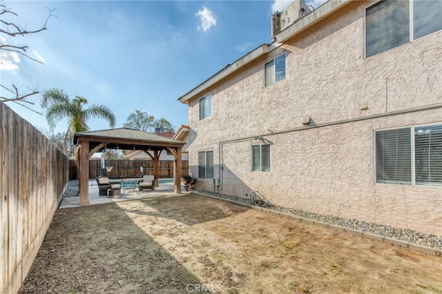 rear view of property featuring a gazebo, stucco siding, a patio, and a fenced backyard