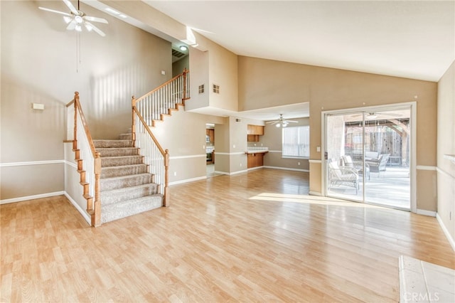 unfurnished living room with ceiling fan, baseboards, light wood-style flooring, and stairs