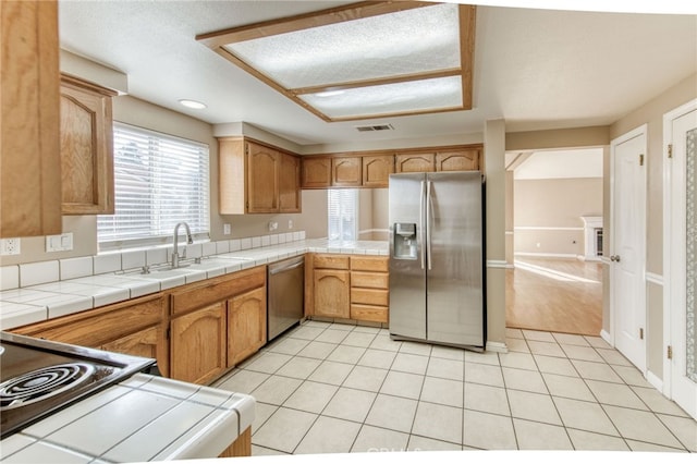 kitchen featuring light tile patterned floors, visible vents, a sink, tile counters, and appliances with stainless steel finishes