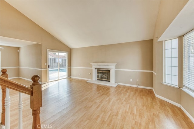 unfurnished living room featuring a glass covered fireplace, baseboards, lofted ceiling, and light wood-style floors