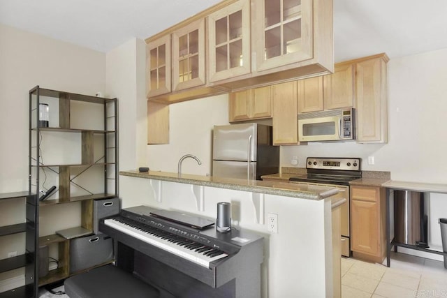 kitchen with light stone countertops, light tile patterned flooring, light brown cabinetry, stainless steel appliances, and glass insert cabinets