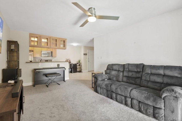 living area with baseboards, light colored carpet, and a ceiling fan