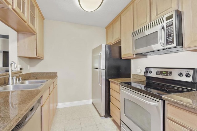 kitchen with a sink, baseboards, appliances with stainless steel finishes, and light brown cabinets