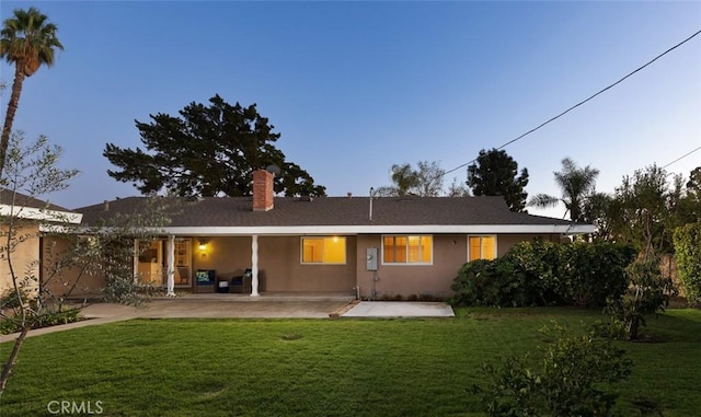 back of property featuring a yard, a patio area, a chimney, and stucco siding