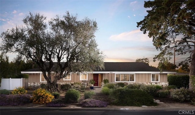 ranch-style home featuring stone siding, board and batten siding, and fence