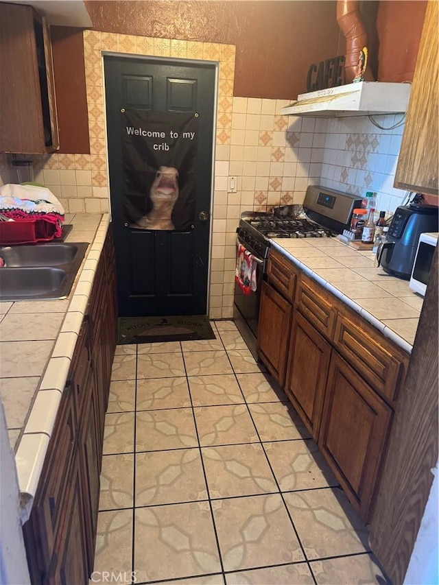 kitchen with tile countertops, ventilation hood, a sink, gas range, and tile walls