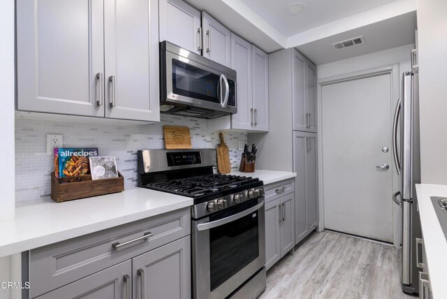 kitchen with light wood finished floors, visible vents, gray cabinetry, and stainless steel appliances