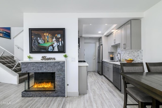 kitchen with backsplash, gray cabinetry, appliances with stainless steel finishes, a fireplace, and a sink