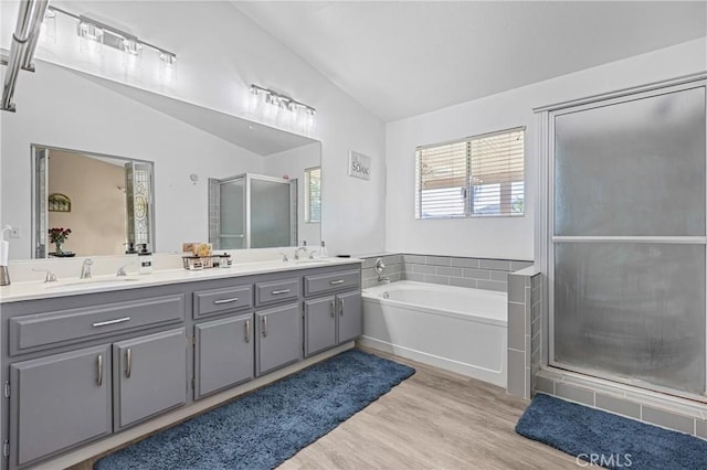 full bath with a bath, a stall shower, lofted ceiling, and a sink