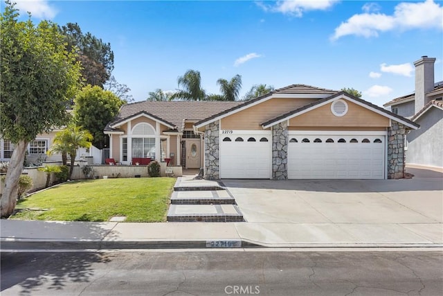 view of front of property featuring a tiled roof, concrete driveway, a front yard, a garage, and stone siding