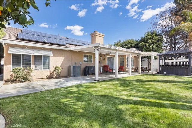 back of house with roof mounted solar panels, stucco siding, a yard, a patio area, and a pergola