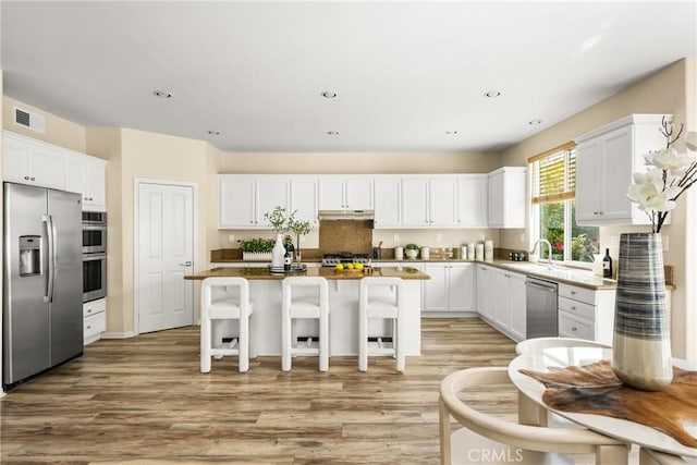 kitchen featuring visible vents, under cabinet range hood, a center island, appliances with stainless steel finishes, and white cabinets