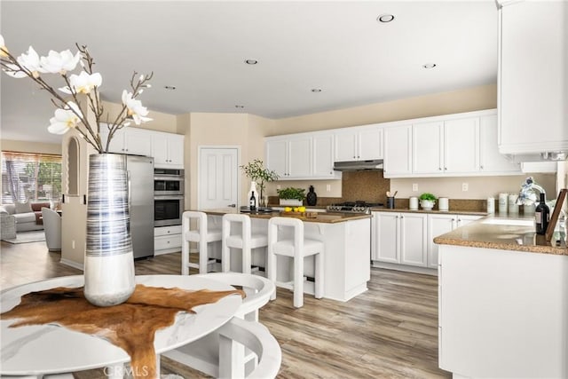 kitchen with a kitchen island, a sink, under cabinet range hood, appliances with stainless steel finishes, and white cabinetry