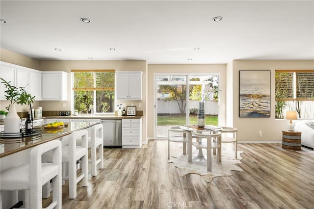 kitchen with plenty of natural light, white cabinetry, light wood-style floors, and stainless steel dishwasher