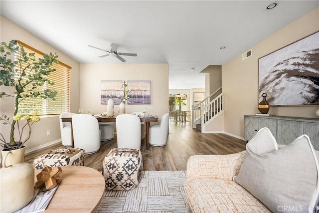 living room featuring visible vents, wood finished floors, stairway, baseboards, and ceiling fan