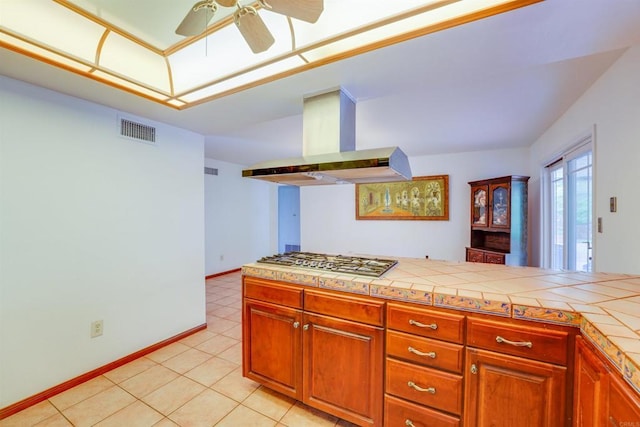 kitchen with visible vents, baseboards, tile counters, island exhaust hood, and stainless steel gas stovetop