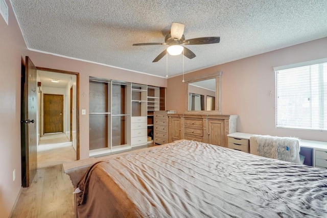 bedroom featuring light wood-style flooring, a ceiling fan, visible vents, and a textured ceiling