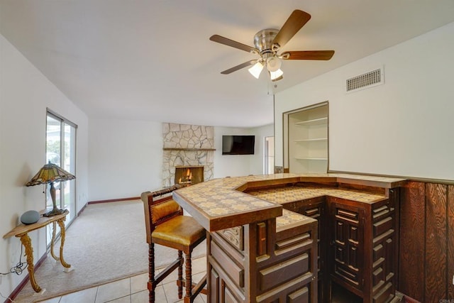 tiled dining room featuring visible vents, carpet floors, a fireplace, baseboards, and ceiling fan